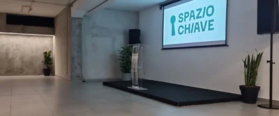 Sala con palco, leggio e schermo con logo Spazio Chiave – location eventi Milano